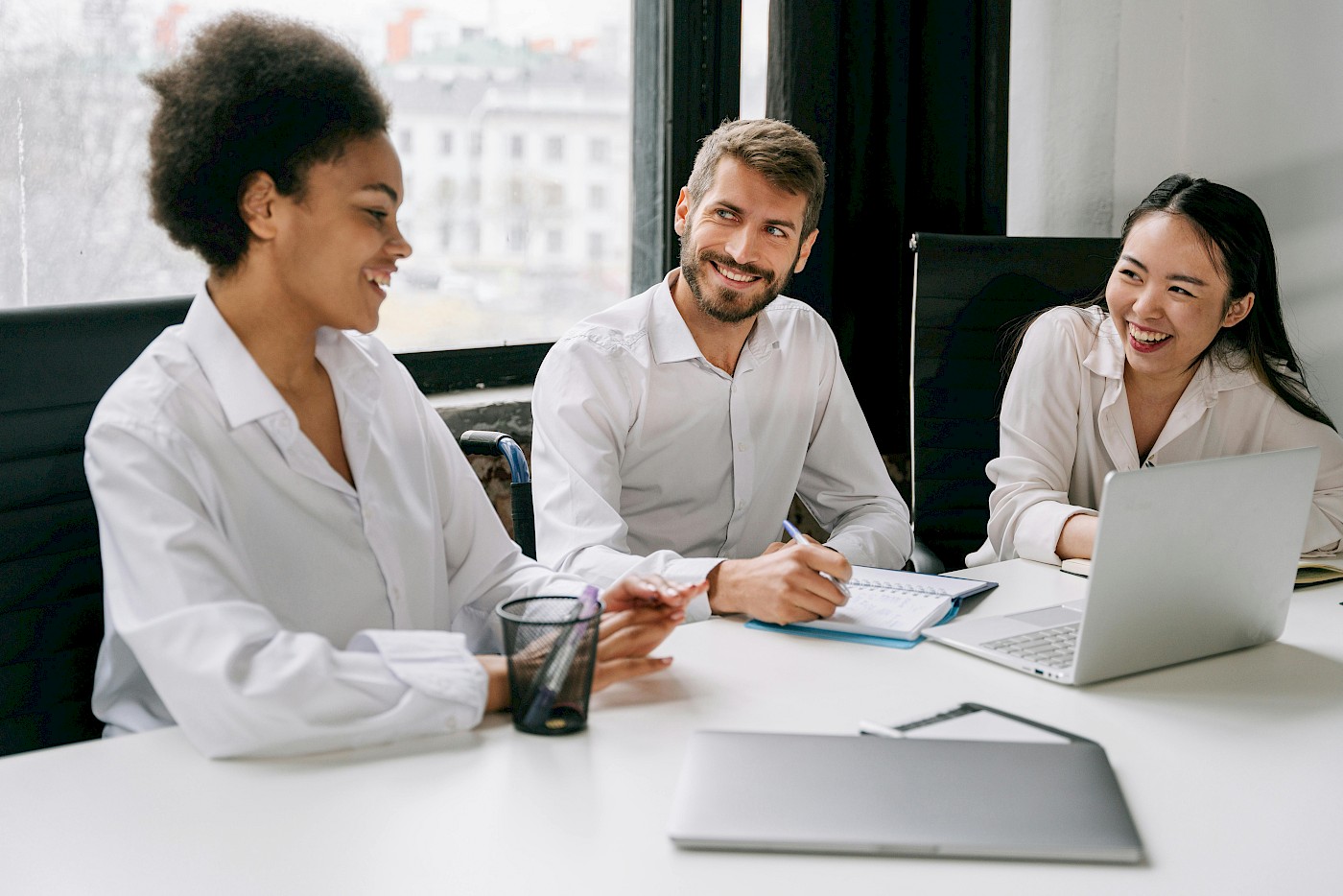 Trois collègues échangent autour d’une table dans un environnement professionnel.