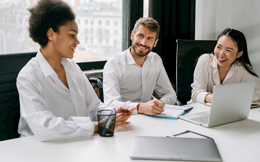 Trois collègues échangent autour d’une table dans un environnement professionnel.